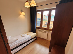 Pokój typu Studio 2+1, wyposażony jest w dwie niezależne sypialnie. W głównej znajduje się zaścielone łóżko, biurko z telewizorem i lodówką, szafa oraz stolik z krzesłami. W mniejszym pokoju jest zaścielone łóżko, szafka nocna z lampką oraz szafa.