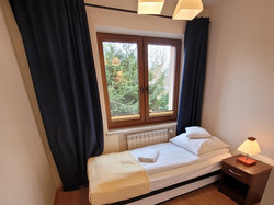 Pokój typu Studio 2+1, wyposażony jest w dwie niezależne sypialnie. W głównej znajduje się zaścielone łóżko, biurko z telewizorem i lodówką, szafa oraz stolik z krzesłami. W mniejszym pokoju jest zaścielone łóżko, szafka nocna z lampką oraz szafa.