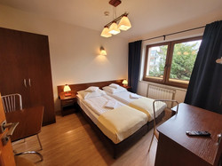 Pokój typu Studio 2+1, wyposażony jest w dwie niezależne sypialnie. W głównej znajduje się zaścielone łóżko, biurko z telewizorem i lodówką, szafa oraz stolik z krzesłami. W mniejszym pokoju jest zaścielone łóżko, szafka nocna z lampką oraz szafa.