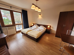 Pokój typu Studio 2+1, wyposażony jest w dwie niezależne sypialnie. W głównej znajduje się zaścielone łóżko, biurko z telewizorem i lodówką, szafa oraz stolik z krzesłami. W mniejszym pokoju jest zaścielone łóżko, szafka nocna z lampką oraz szafa.